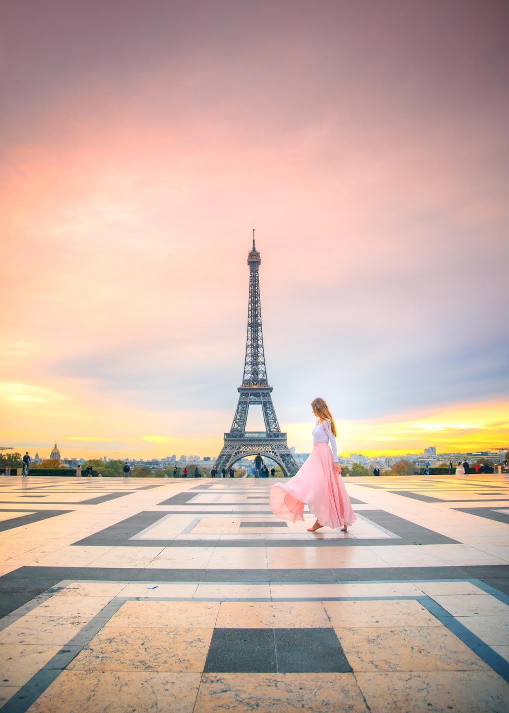 Vivid pink sunset over the Eiffel Tower with a woman in a pink, flowing dress at Place du Trocadero.