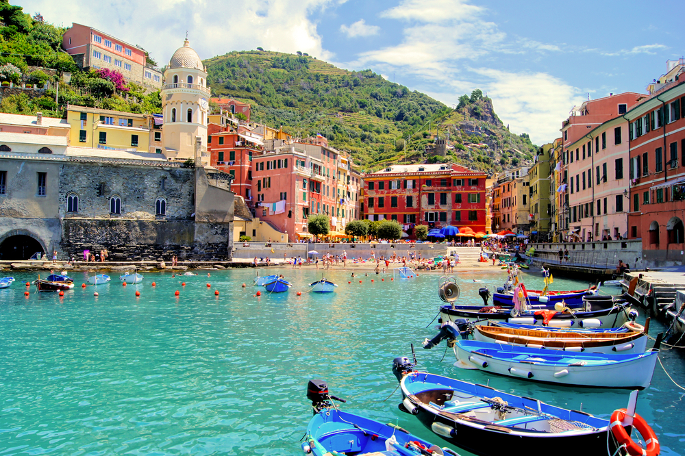 Small motorboats docked in a harbor near a beach and colorful buildings in Cinque Terre.