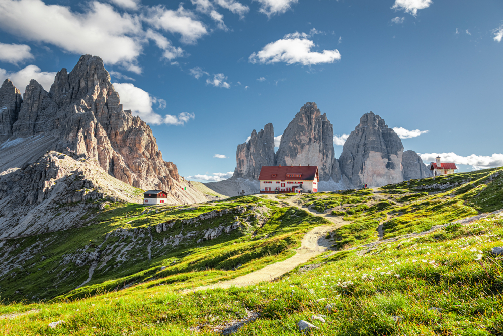 Path leading to buildings dotted on hills near the rugged Eastern Dolomites.