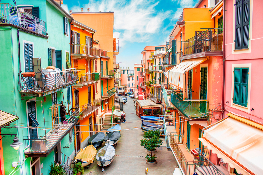 View down a colorful alley in Cinque Terre with boats on the street.