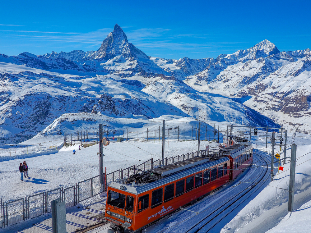 a red train passing through the Zermatt Switzerland in the winter time. there is plenty of snow covering the mountains and it looks magical 