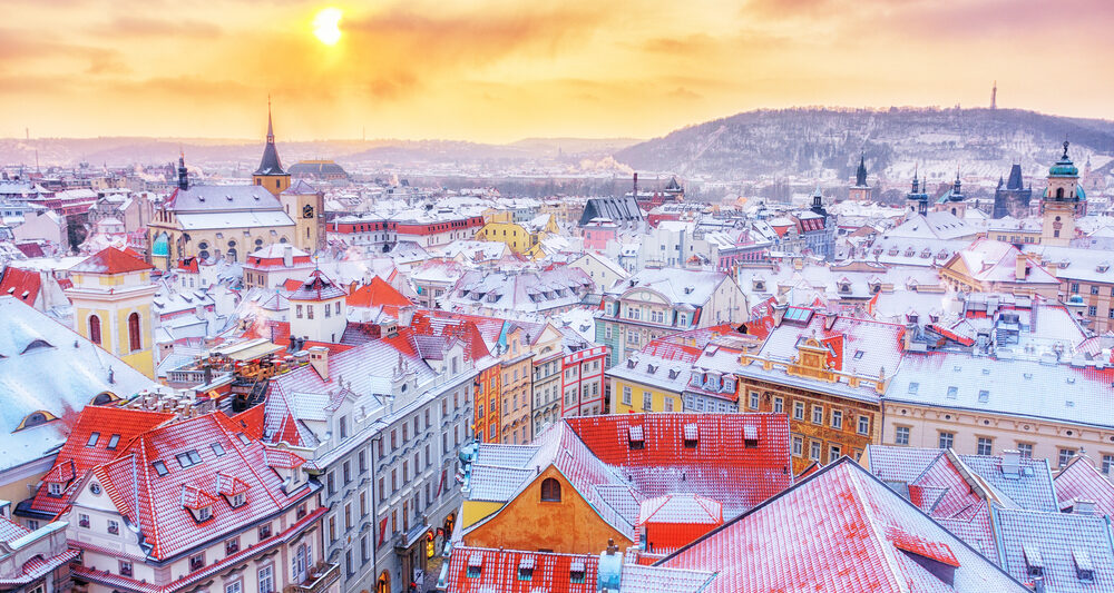 a beautiful photo of one of the best places to visit in Europe in February at sunset. there is snow on all the buildings and plenty of colorful buildings