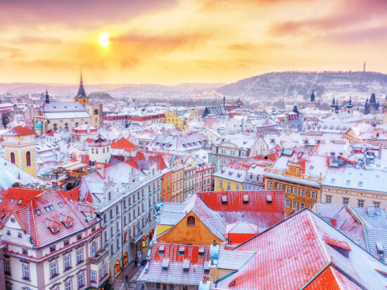 a beautiful photo of one of the best places to visit in Europe in February at sunset. there is snow on all the buildings and plenty of colorful buildings