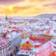 a beautiful photo of one of the best places to visit in Europe in February at sunset. there is snow on all the buildings and plenty of colorful buildings