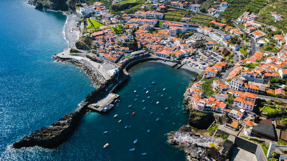 a view of madeira portugal from above. there is a lovely port full of boats and homes, stores, and restaurants on the shore. this is one of the best places to visit in Europe in February 