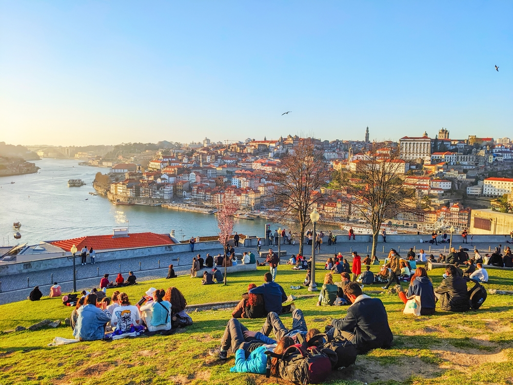 people sitting on the hill in porto Portugal during February. people are wearing coats, but not to bundled up, and the river is calm and beautiful 
