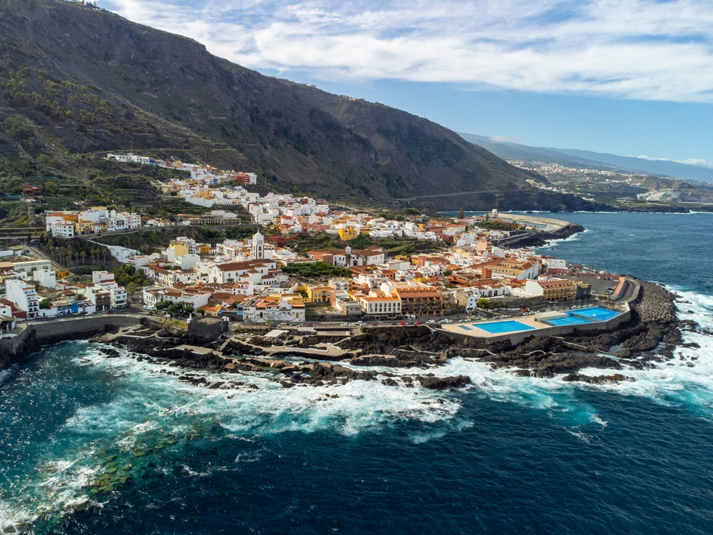 a view of the town of Tenerife, Spain during the winter. there is an ocean, small town, and beautiful mountains in the back round. 