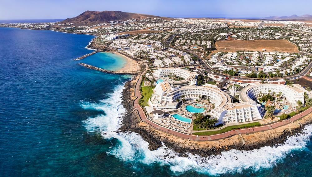 Lanzarote, one of the best places to visit in europe in march, curved resorts can be seen along the coastline, waves are crashing onto the shore