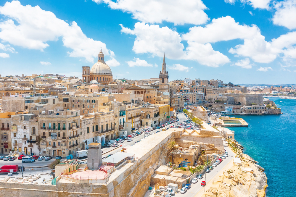 ocean on the right, malta town on the left, cars are parked along buildings and coastline