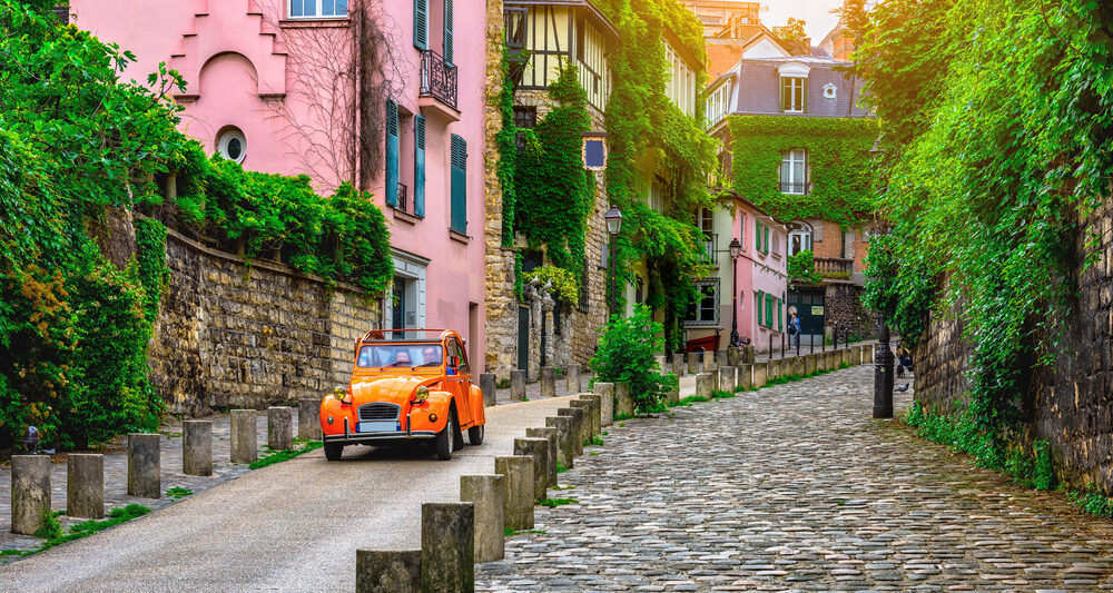 Car on cute european street with pink house in the background and green trees