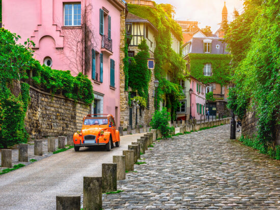 Car on cute european street with pink house in the background and green trees