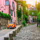 Car on cute european street with pink house in the background and green trees