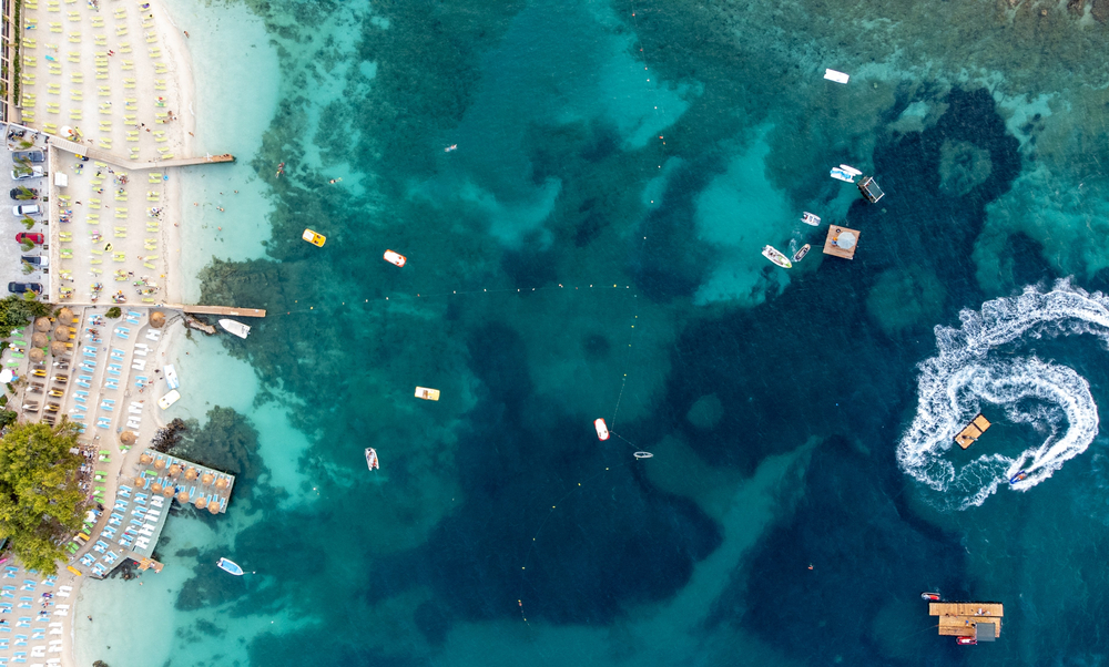 a drone photo of the Albanian Riviera. there are beach chairs in the sand, boats out in the water, and the prettiest white sand. 