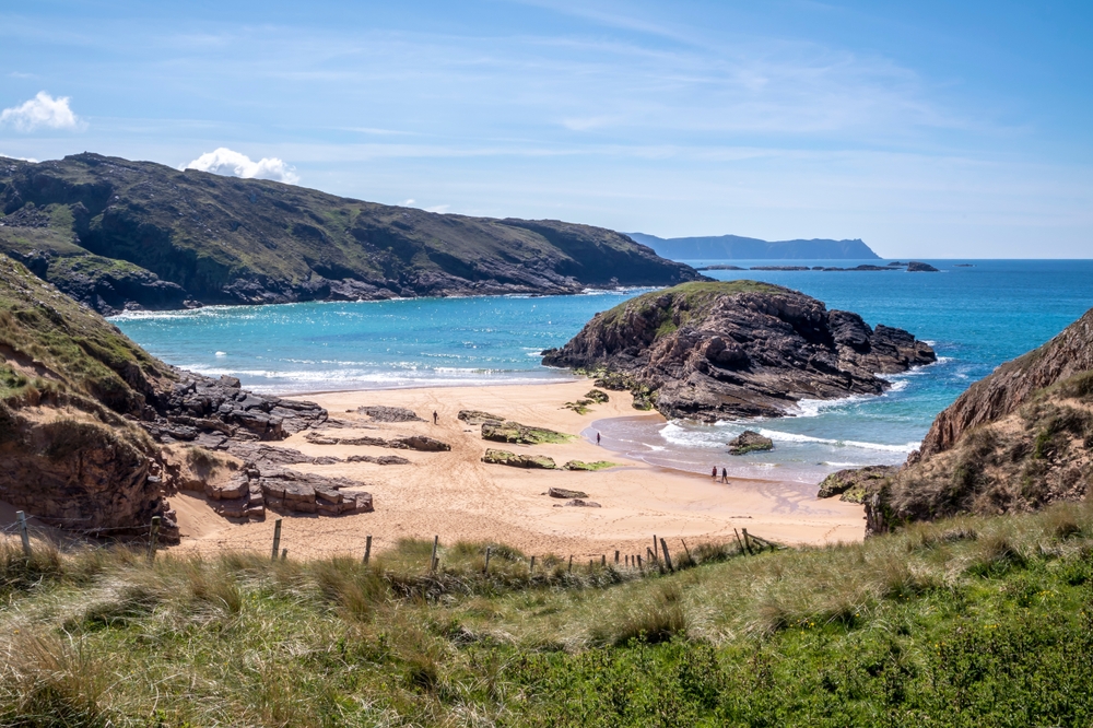 an beach in Ireland during the summertime. the beach is almost empty with just a few people exploring the sea rocked and hanging out in the sand 