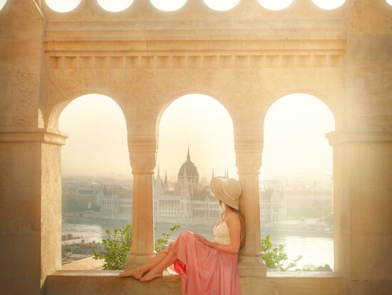 woman sitting in a pink skirt with buildings in Budapest, Hungary in the background at sunrise