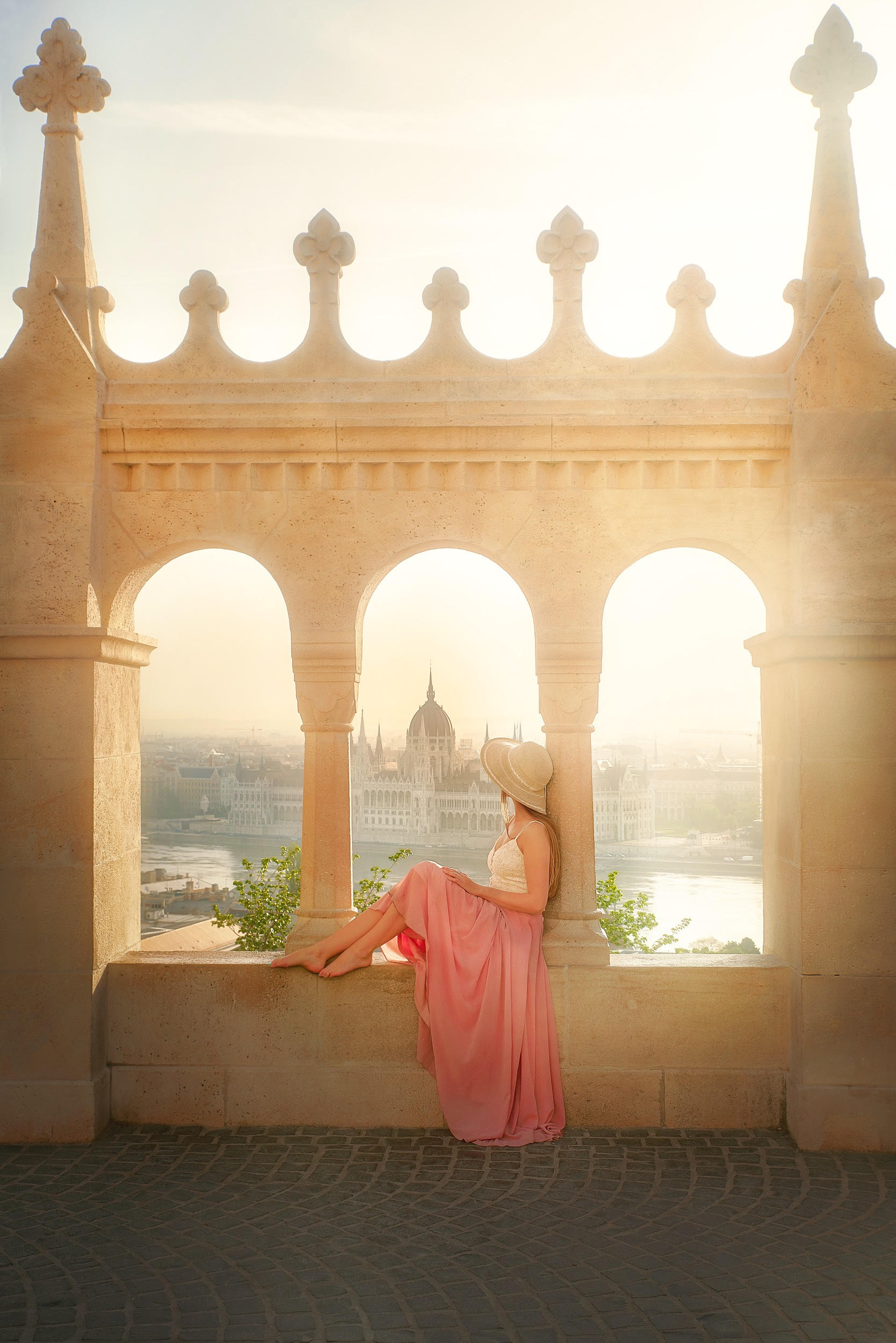 Girl sat above a European skyline looking out over the river and city in the distance. The article is about the  best time to visit Europe. 