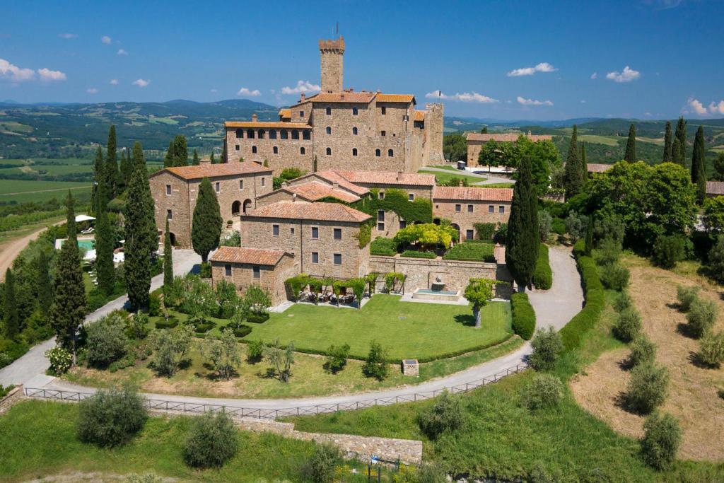 a castle with a turret and lots of chuildings spread on a hillside with trees around. 