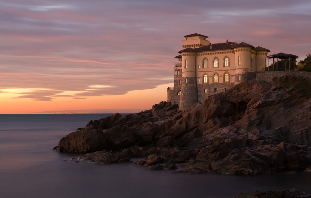 Castello del Boccale in Livorno, Tuscany at sunset. The castle is white with turrets and sits on a rocky outcrop.  