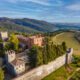 Tuscan castle with brown stone perched on a cliff with wine fields below and green mountains in the background