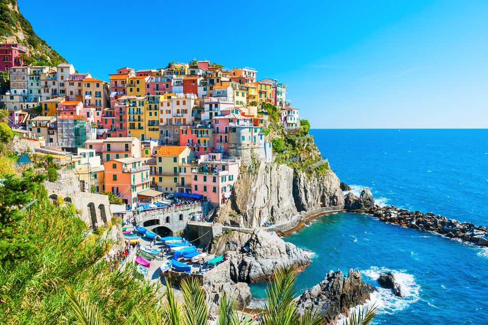 Brightly colored buildings built on the side of a rocky cliff with greenery growing on it on the side of the ocean one of the best places to visit in Europe in May