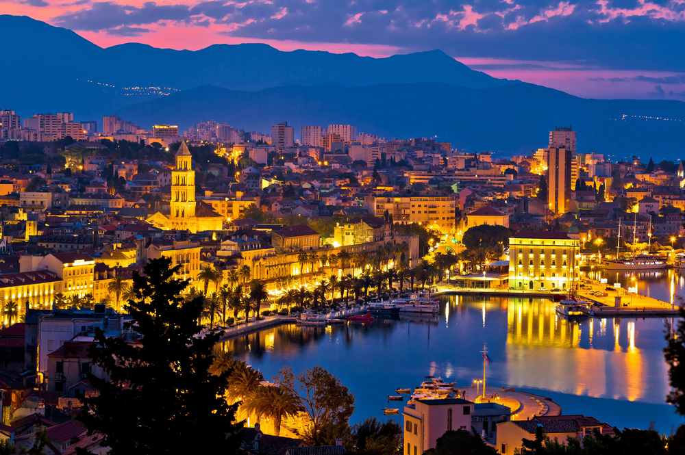 a beautiful town in croatia in the winter time. ti is a sunset and the clouds are pink and blue and the orange bright lights are ill mating the sky. this is one of the best places to visit in Europe in February. 