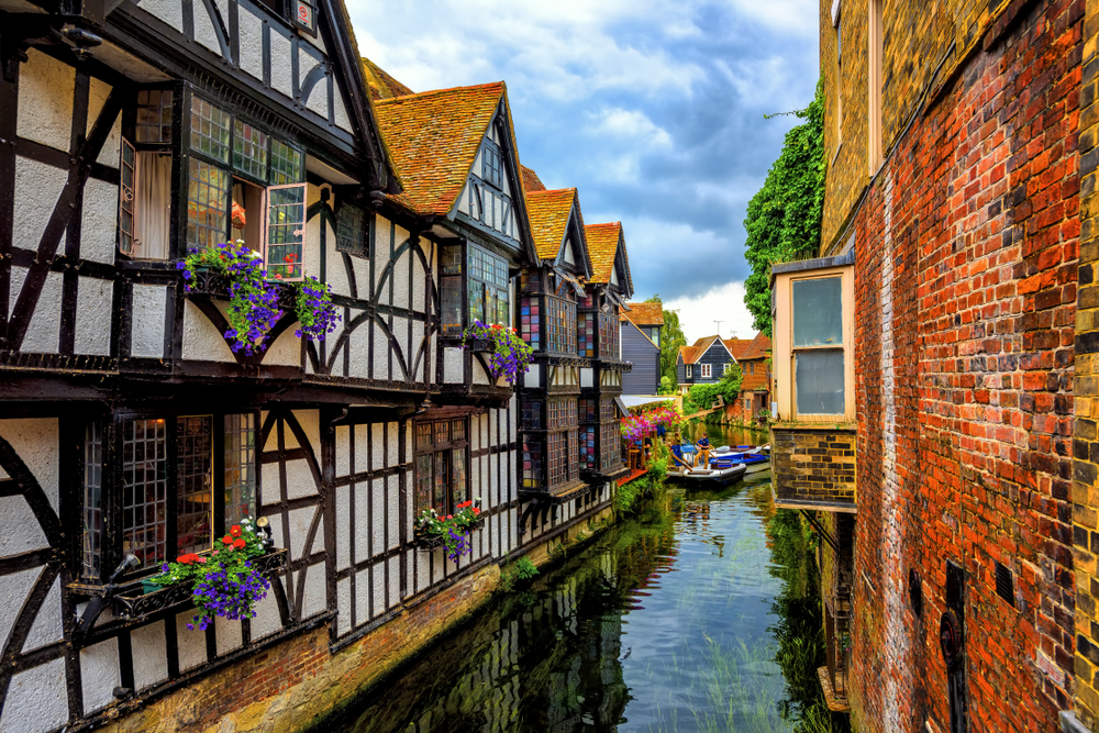 Medieval half-timber houses and Stour river in Canterbury Old Town, Kent. The houses are balck and white and there are flowers in boxes at the window.