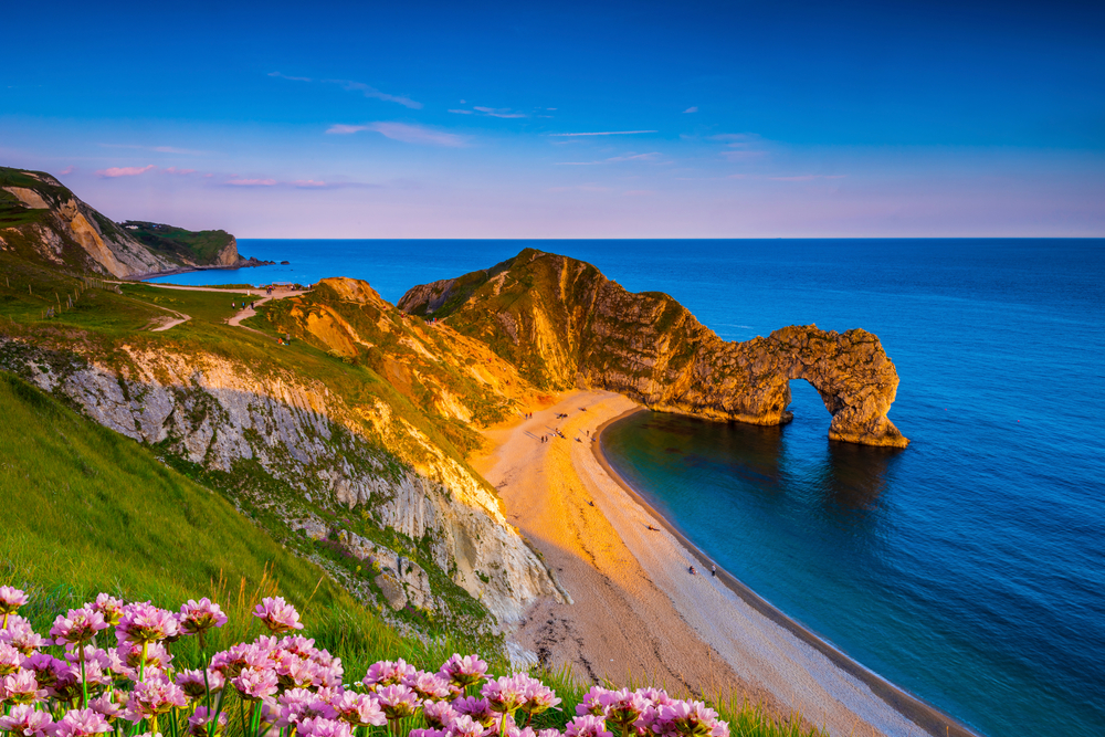 The sun goes down on the Jurassic coast and Durdle Door in Dorset with Seak Pink Trift growing on the top of the cliff in the foreground. One of the places to go in souther England. 