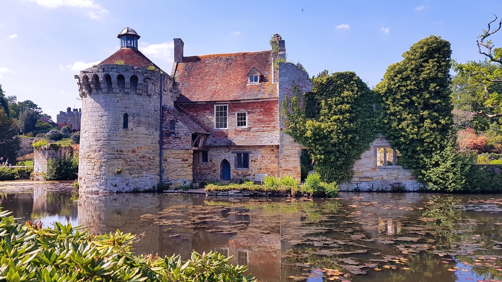 Scotney Castle with a round turet with the a moat in front of it. there is greenary on the castle. It's one of the places in southern england