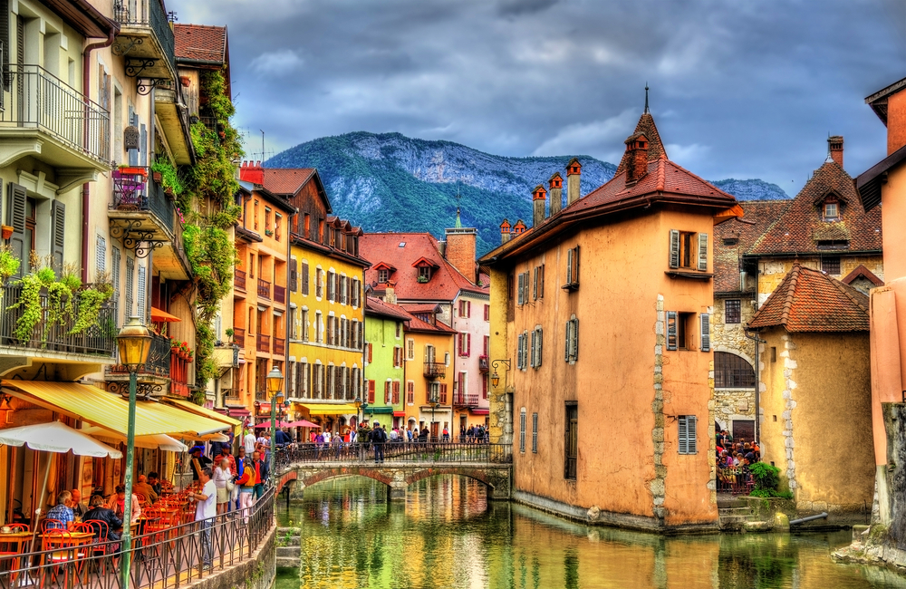 View of the old town of Annecy. You can see canals with houses around and a mountain in the background.  
