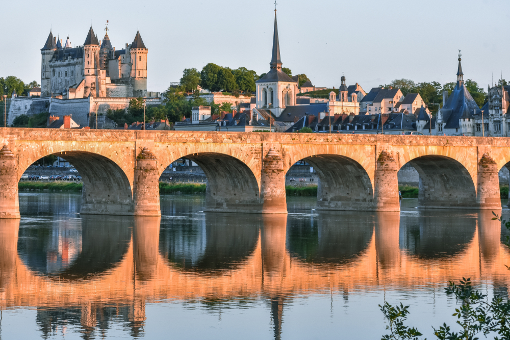 Views of the city of Saumur from the riverbank at dusk, with the castle in the background.