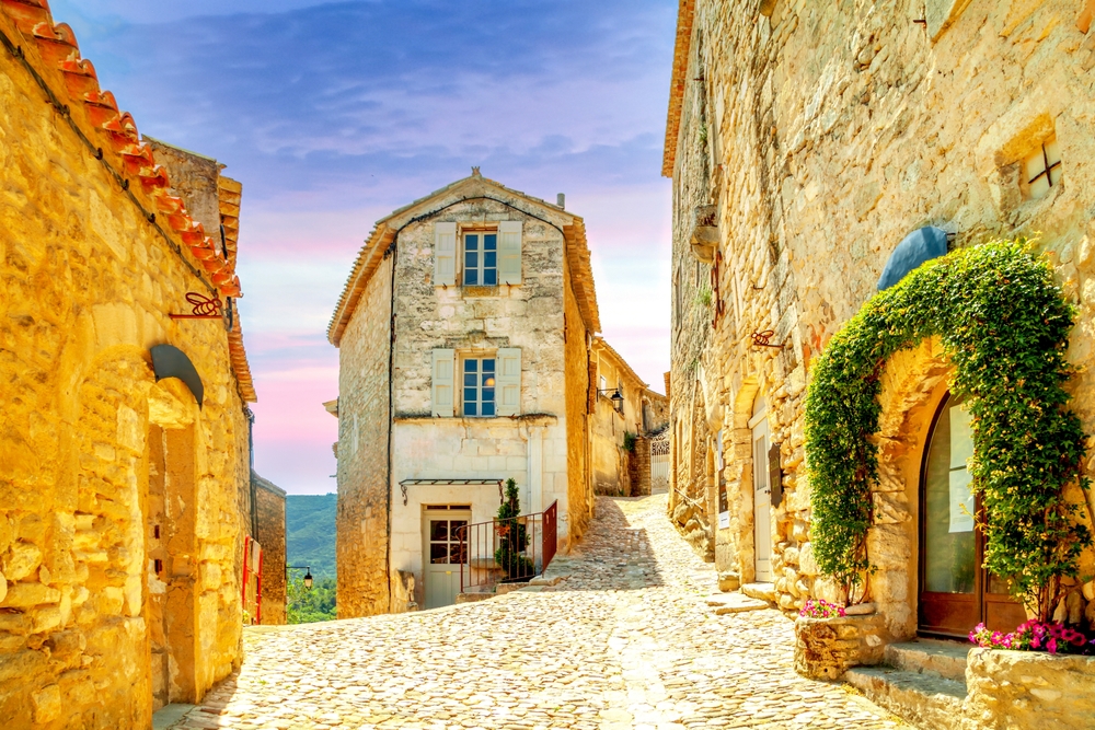 Old city of Lacoste, France. Showing a cobbled street with buildings some covered in greenery. 