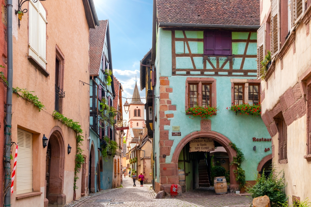 A colorful narrow cobblestone alley and street of shops and cafes in the medieval Alsatian Village of Riquewihr, France