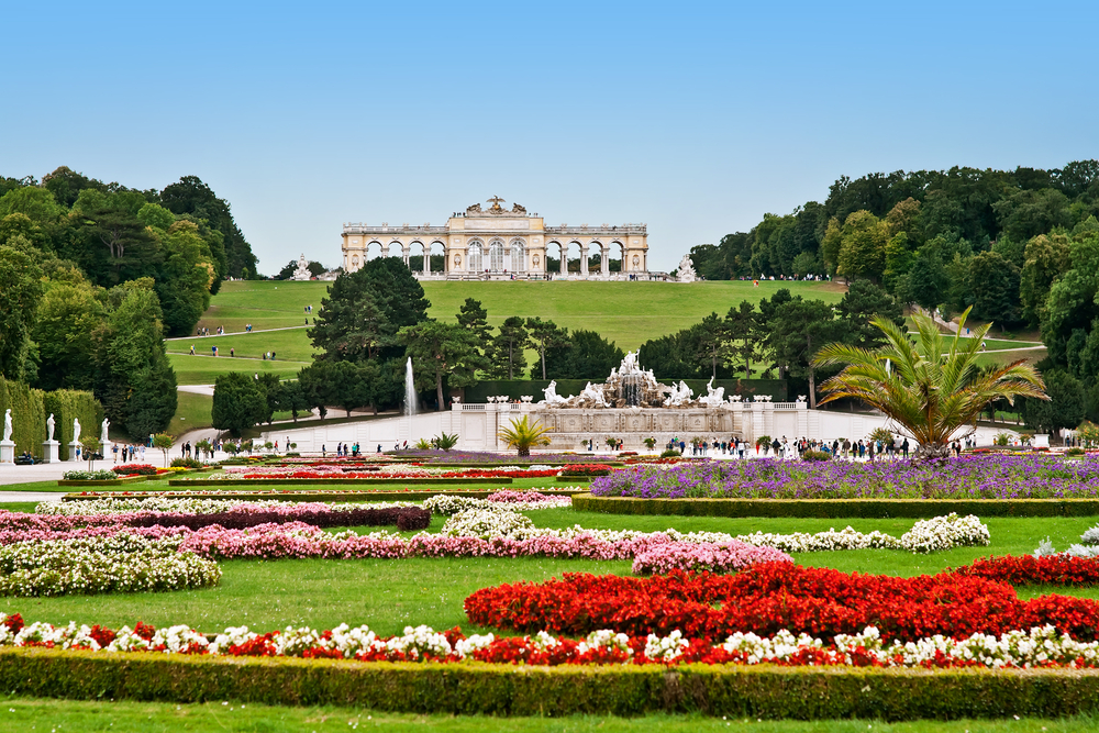 A palace building looking down at elaborate manicured gardens with flowers in all colors blooming one of the best places to visit in Europe in May