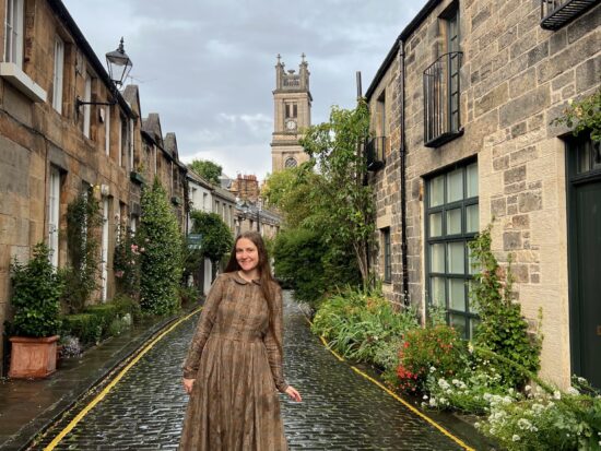a girl in brown dress standing on onne of the many streets in Edinburgh