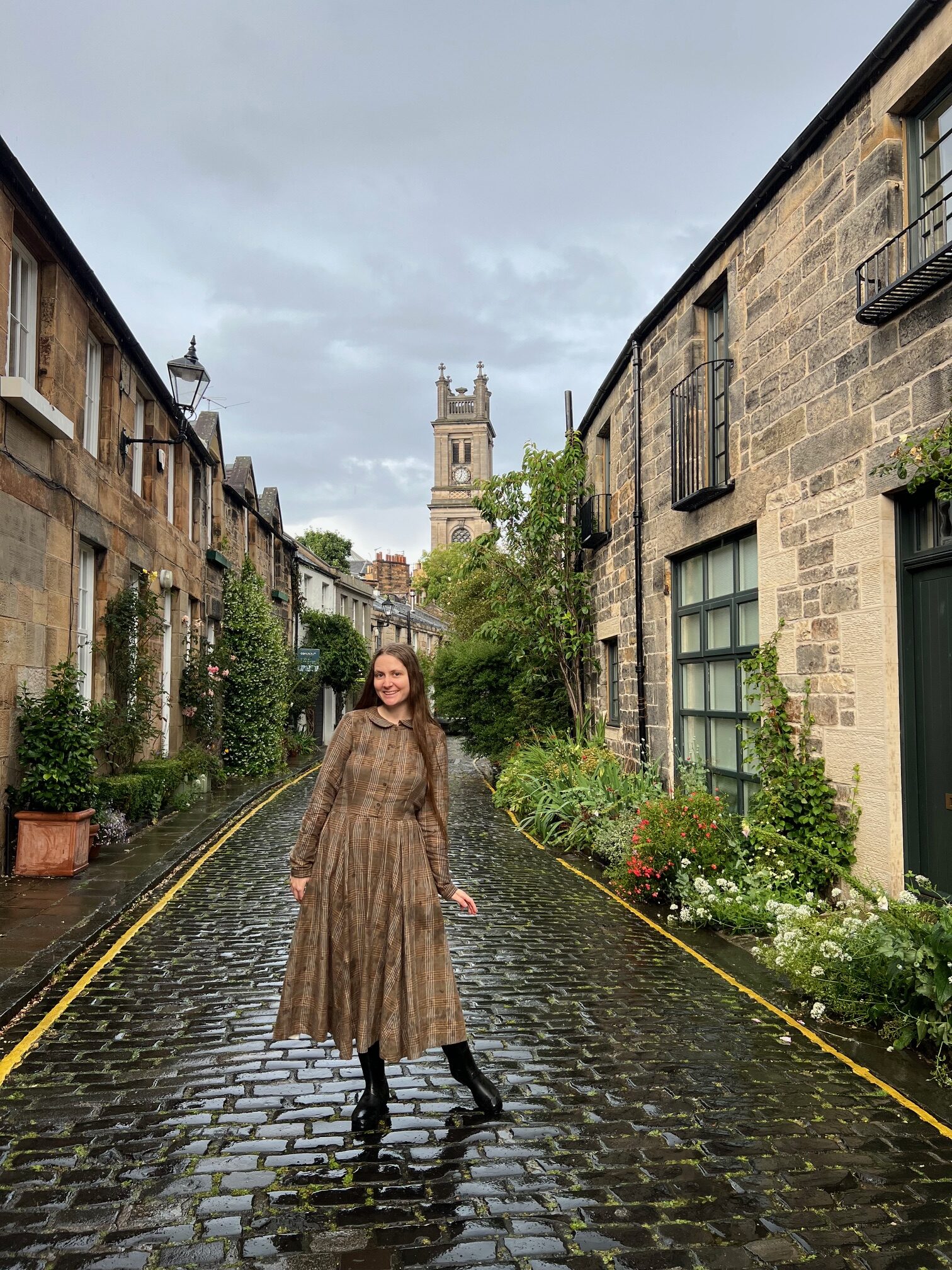 a girl in a brown dress standing in front of circus lane  with cobblestone and stone buildings