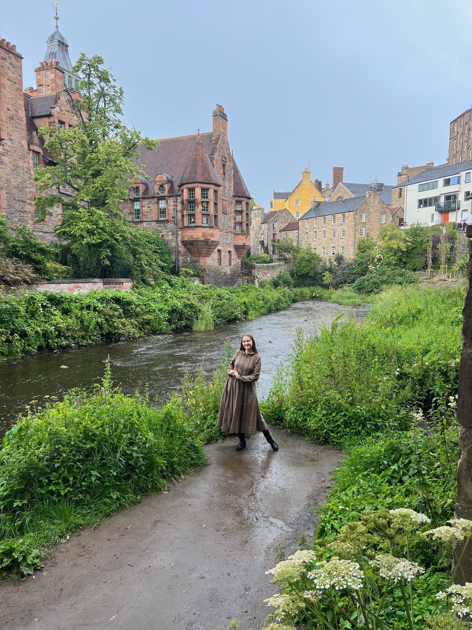 A girl in a Brown dress standing in front of the River with the Castle in the background at Dean Village
