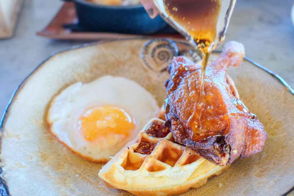 a duck confit served over a waffle with egg and a syrup