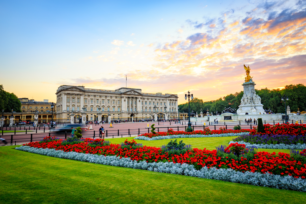 Buckingham palace in the summertime with the flower gardens and cotton candy sky