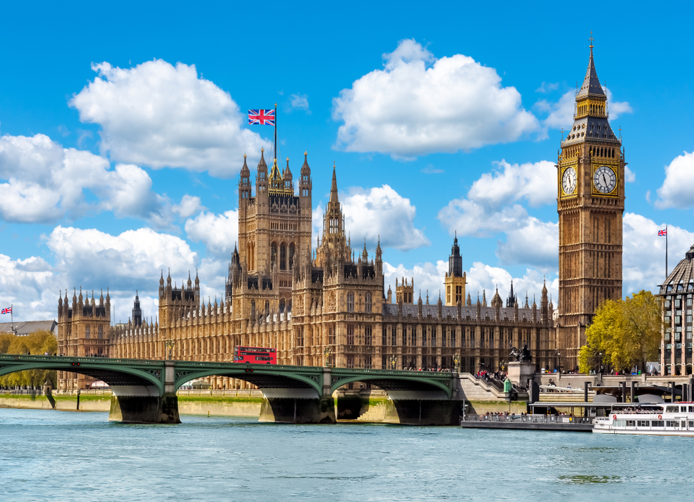 The iconic clocktower known as BIg Ben and the Parliament building with the river and a red London bus passing by