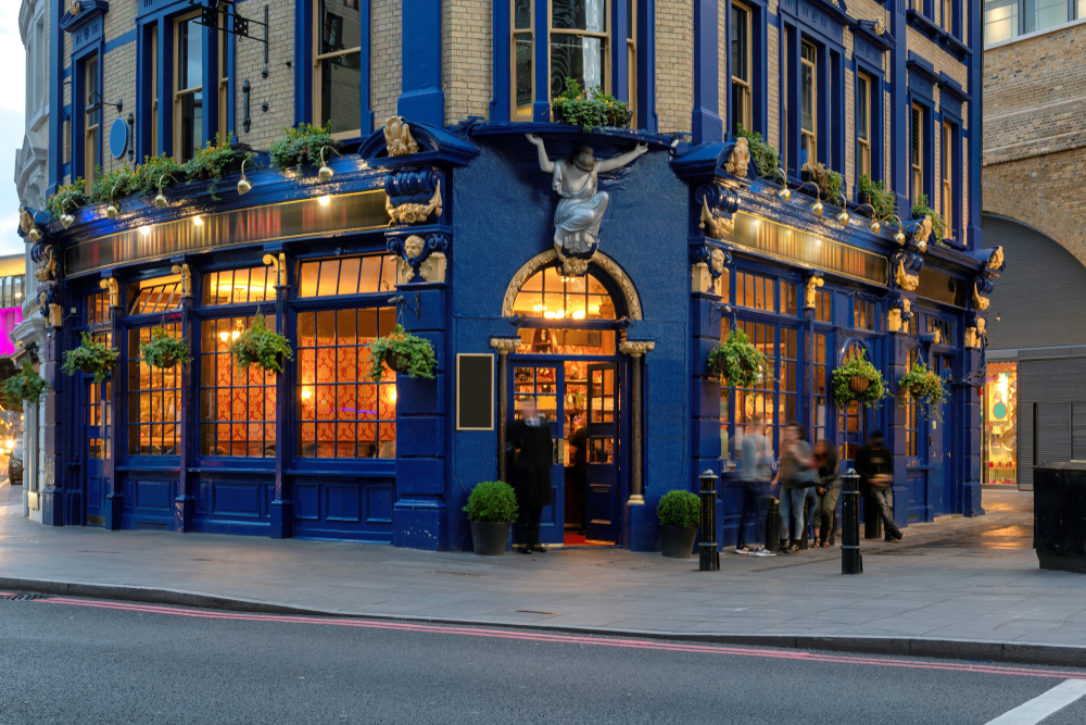 A traditional English pub with dark blue and gold along with green shrubs