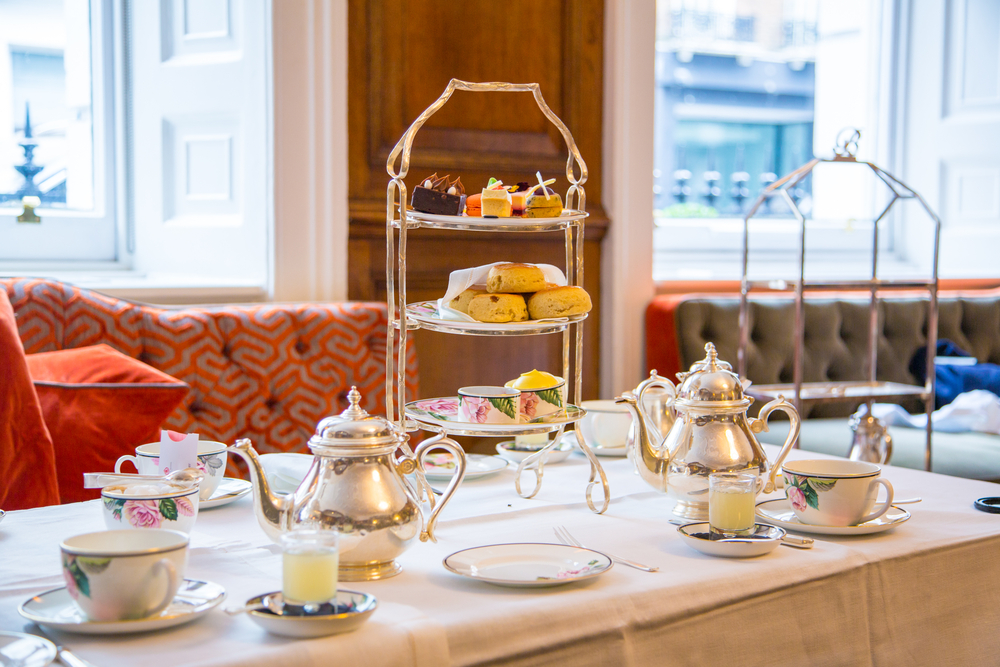 High tea service with gold tiered trays with flowered tea cups and. silver pots with scones is one of the things to do in 3 days in London