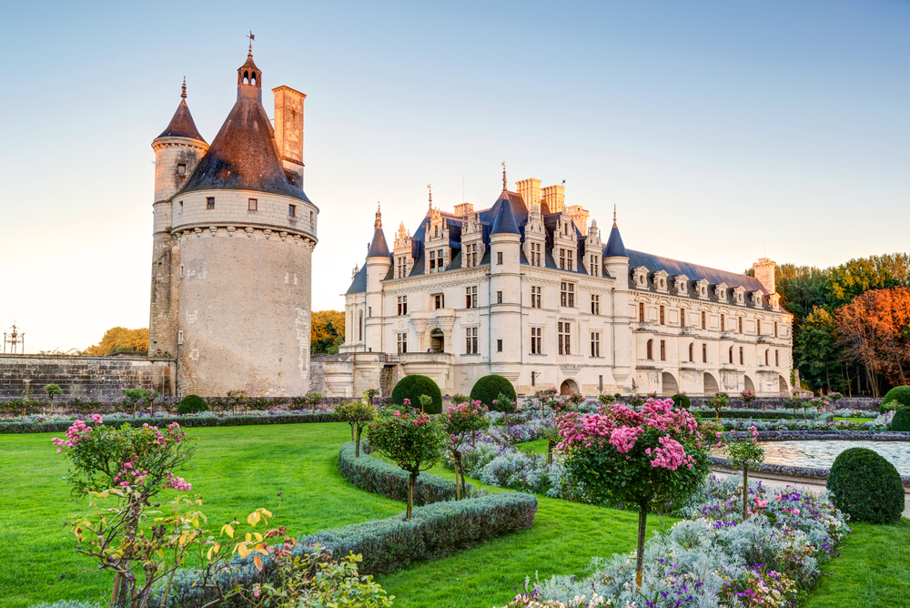 Golden hour at Château de Chenonceau with a round tower and pretty formal gardens with flowers.