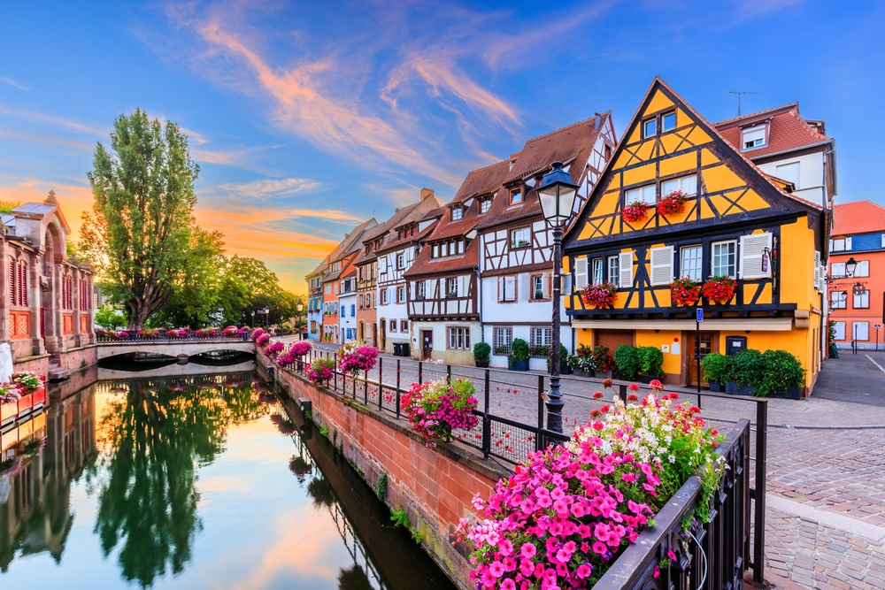 Sunset over colorful wood-timbered buildings along a canal with flowers in Colmar on a France road trip.
