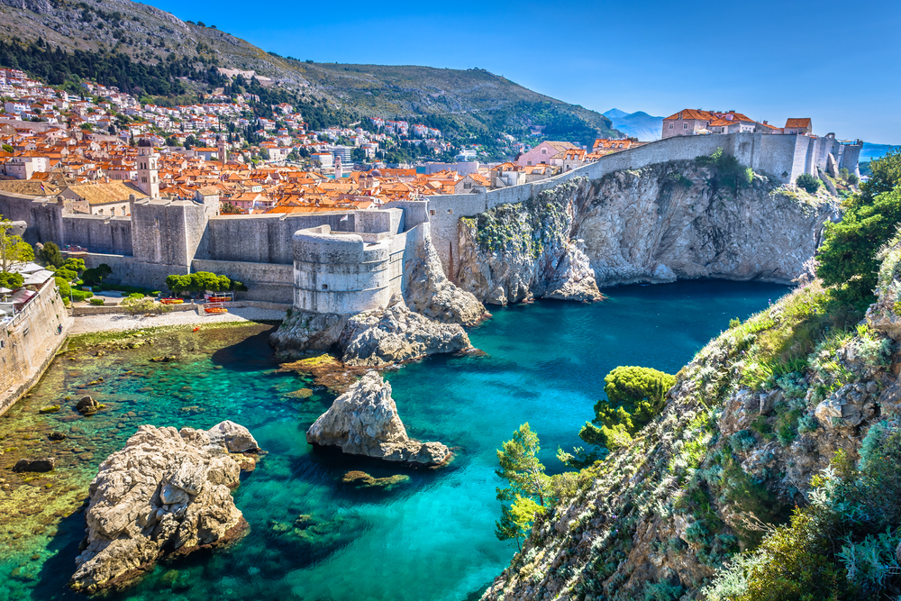 View of the bright blue water along the coast of Dubrovnik with walls around the city.
