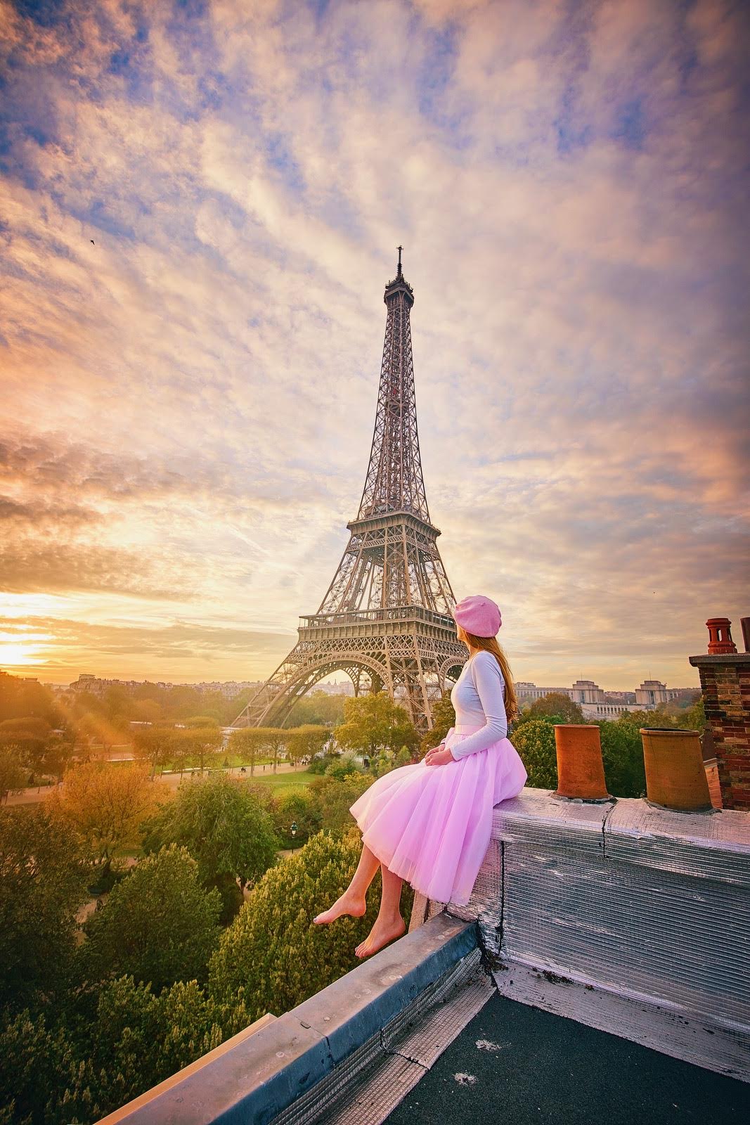Vivid pink sunset over a woman in a pink skirt and beret sitting on a rooftop overlooking the Eiffel Tower in France.