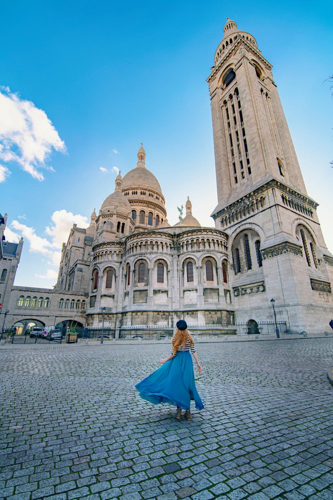Woman in a flowing blue skirt standing under the white Sacre Couer basilica in Paris on a France road trip.
