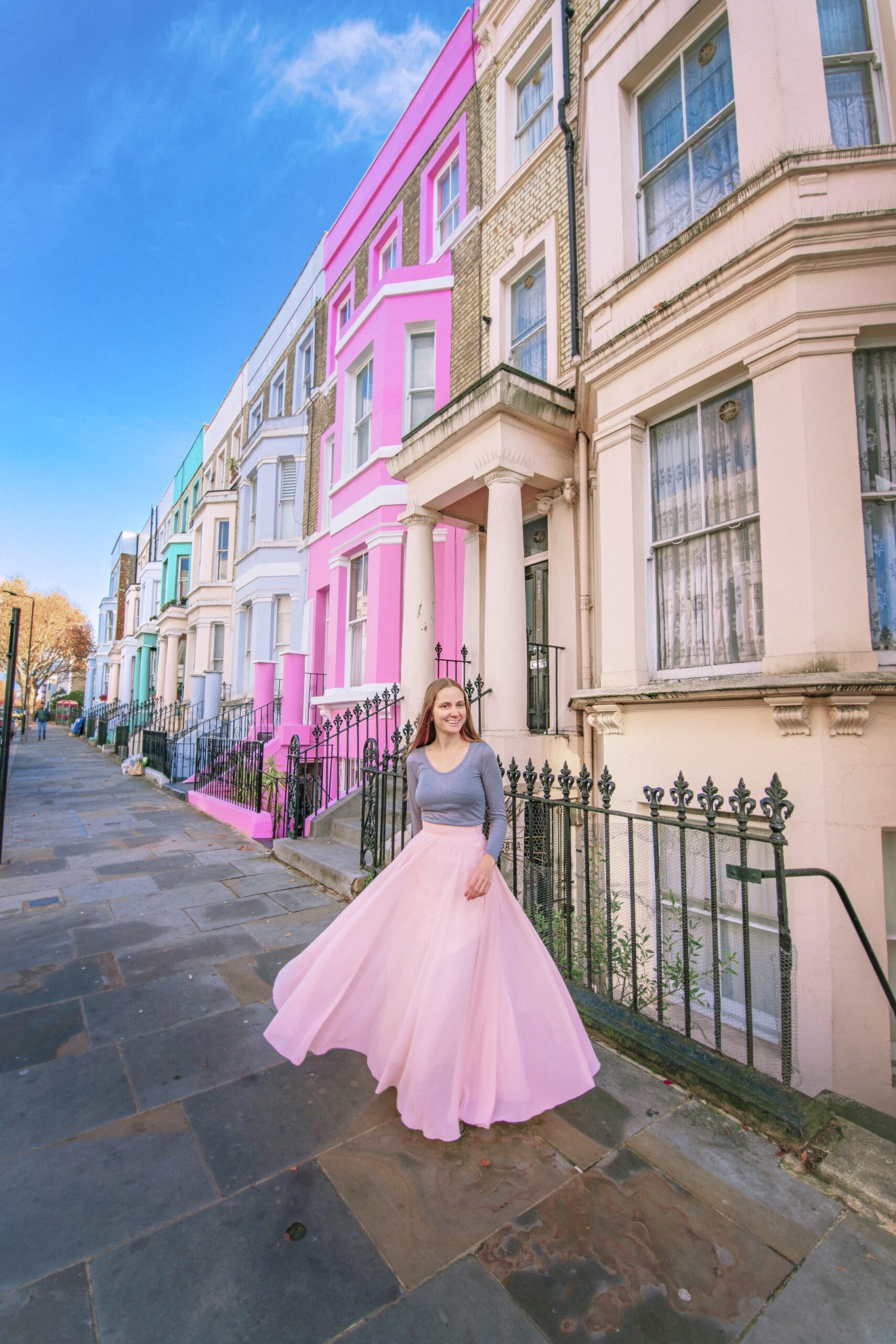a girl in a pink skirt standing in front of the colorful homes in nottinghil
