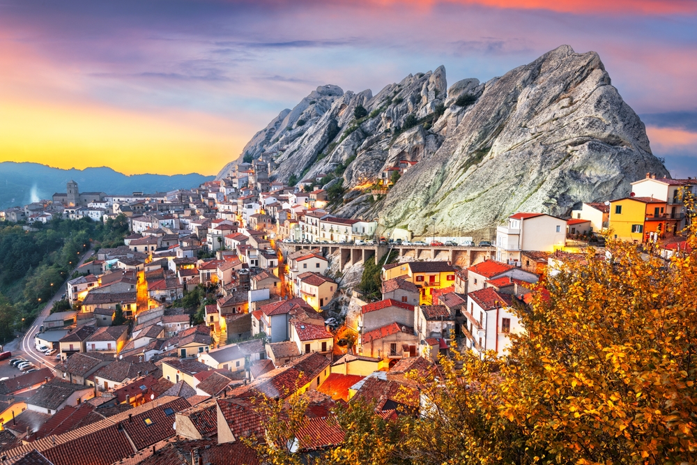 Vivid sunset over the lit up town of Pietrapertosa along the top of a rugged mountain.