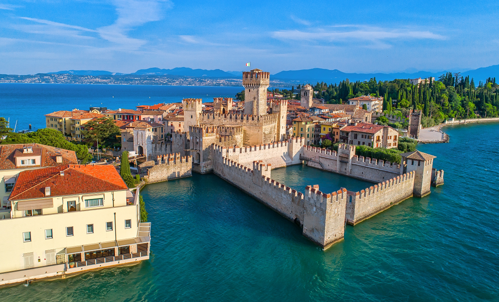 Aerial view of Scaligero Castle with stone walls jutting out into the water on a sunny day.