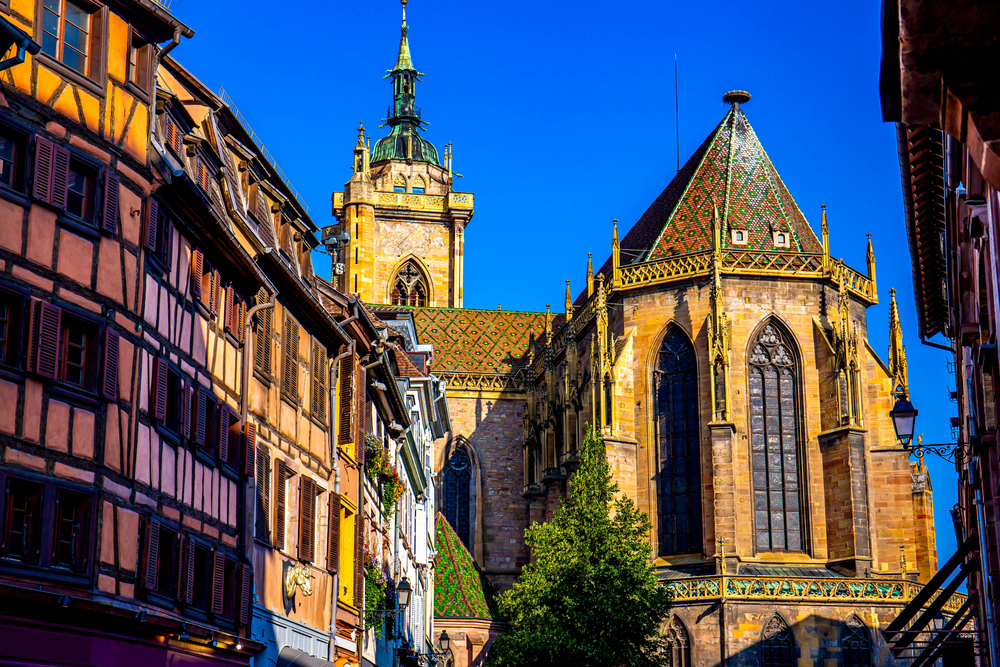 Exterior of St. Martin's Church at golden hour next to wood-timbered buildings.